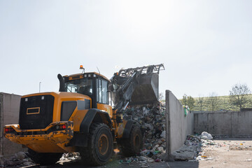 Yellow skid steer loader moving wooden waste material, shaking out a scrap grapple on the garbage...