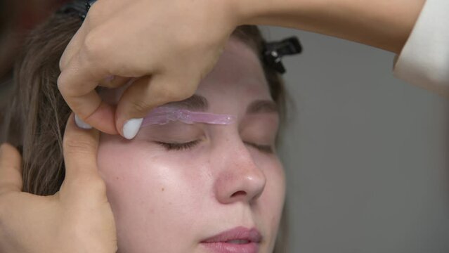Correction of eyebrow shape with hot wax close-up. An eyebrow artist applies wax to the eyebrow of a woman's face and removes the hardened pink wax. Wax correction of eyebrow shape