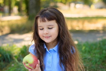 Happy kid eating fruits from picnic basket sitting on the green grass