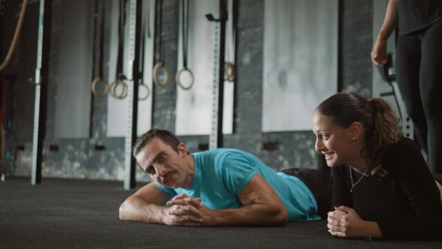 Exhausted sportsman and sportswoman finish training in plank position getting sign from female personal trainer, tired lying on floor in gym