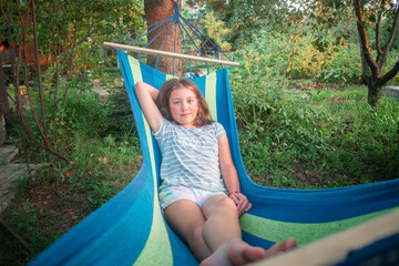 A pretty girl is lying in a hammock in the garden.