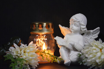 Sympathy card with an angel figurine, votive candle and flowers on black background