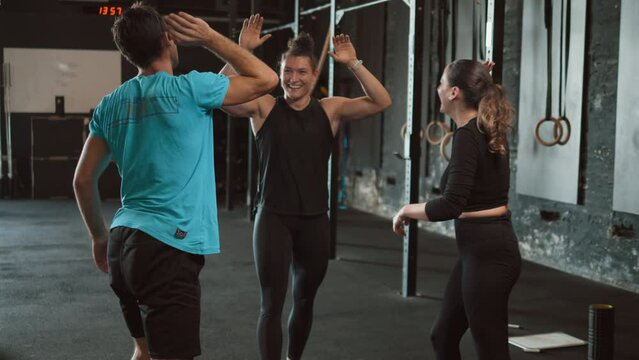 Cheerful female personal trainer winning and greeting athlete happy clients after successful fitness training in the gym