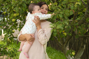 Enveloped by greenery, young mom swings her baby, their faces glowing in mutual admiration and...
