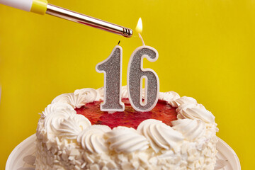 A candle in the form of the number 16, stuck in a festive cake, is lit. Celebrating a birthday or a...