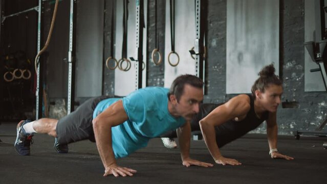 Strong masculine woman and  athlete man doing clapping push-ups in the gym