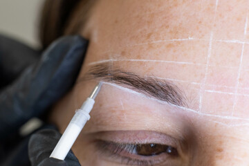 Detailed view of a professional conducting eyebrow mapping on a woman for permanent makeup