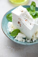 Turquoise bowl with a block of feta cheese and green basil, vertical shot, close-up, selective focus