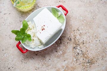 Feta cheese with fresh green basil and olive oil on a beige stone background, horizontal shot, copyspace, high angle view