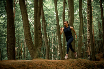 Woman with long dark hair in pony tail running on hilly forest area between tall trees