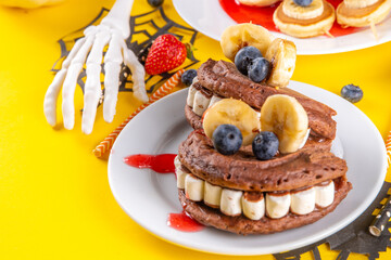 Funny kids breakfast for Halloween. Creative homemade sweet pancakes in form of traditional Halloween monsters and symbols, with fresh berry, chocolate and red syrup