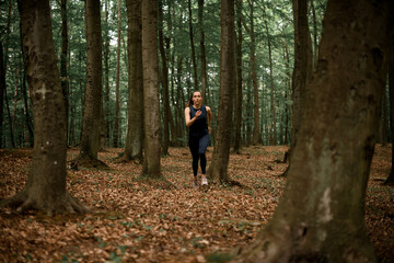 Young female athlete in black sportswear doing morning training in forest among trees.