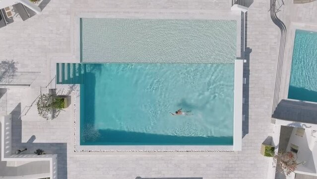 Aerial video of a man swimming in a pool at a hotel on the island of Mykonos