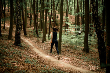 Active young woman doing daily jog on forest path between tall leafy trees
