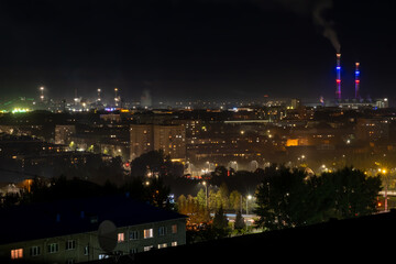 Fototapeta na wymiar The night landscape of the city. Beautiful urban area with houses and boiler room at night. View of the big city from above. Smoking chimneys of boiler rooms on the background of the cityscape.