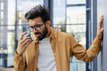 Young man coughing with asthma, businessman outside office building using inhaler.