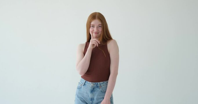 Sweet Caucasian teenage girl is depicted making the shh gesture on a white background. With a gentle smile and a finger placed on her lips, she is gesturing for silence or secrecy.