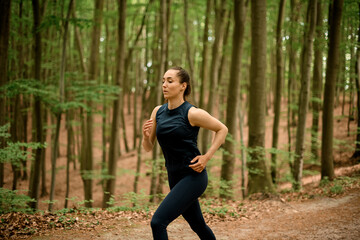 Sporty young woman with long hair runs in forest among trees, side view
