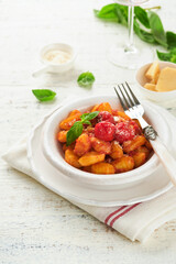 Potato gnocchi. Traditional homemade potato gnocchi with tomato sauce, basil and parmesan cheese on kitchen table on light grey kitchen table background. Traditional Italian food. Top view.