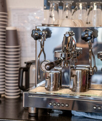 The barista prepares fresh coffee in the coffee machine in the morning in the cafe. There are coffee cups on the table for customers. Coffee machine close-up