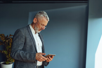 Focused mature businessman working on digital tablet while standing in office