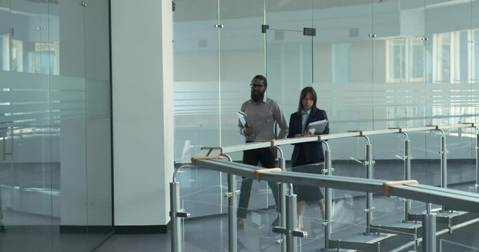Within the office space, an Indian and a Caucasian manager engage in conversation as they walk. Their interaction embodies the camaraderie and exchange of ideas that underlie effective teamwork.