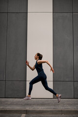 Side view of young woman in comfortable sports clothing running outdoors along the street