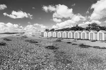 Colorfool beach huts on the shores of Littlehampton Long Beach in Sussex, England, UK; wooden huts on pebbles beach with clouded sky in black and white