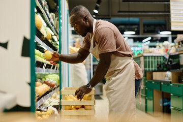 African American merchandiser putting fresh fruits on shelves in supermarket
