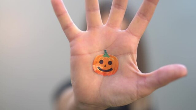 girl opens her palm with an image of an orange pumpkin