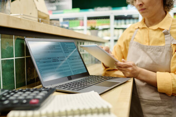 Manager sitting at table with laptop and making financial work in supermarket