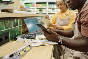 Colleagues sitting at table and using calculate and computer to control the sale of goods in supermarket