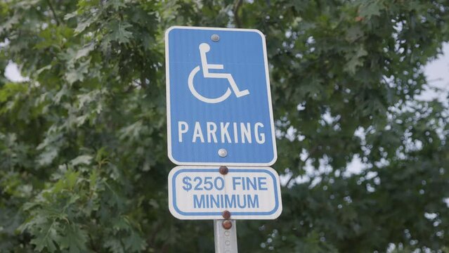 Slow motion handheld close-up shot of blue handicap wheelchair sign with a $250 dollar minimum fine in parking lot