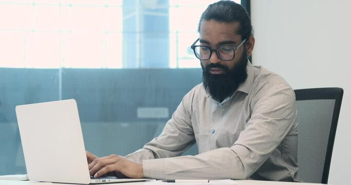 With an air of seriousness, a businessman dedicates himself to typing on laptop within the office. Focused gaze and precise keystrokes reflect his commitment to translating ideas into digital form.