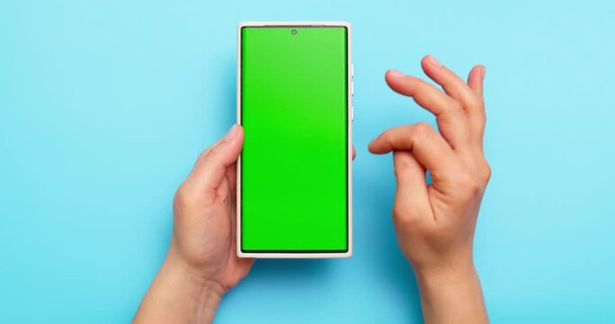 Woman's hands holding smartphone with green screen on blue background