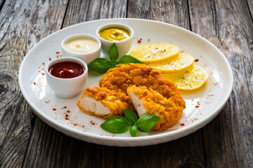 Seared breaded chicken nuggets with mustard, mayonnaise and ketchup on wooden table