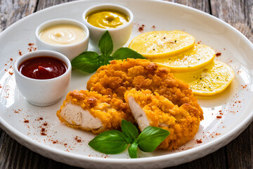 Seared breaded chicken nuggets with mustard, mayonnaise and ketchup on wooden table