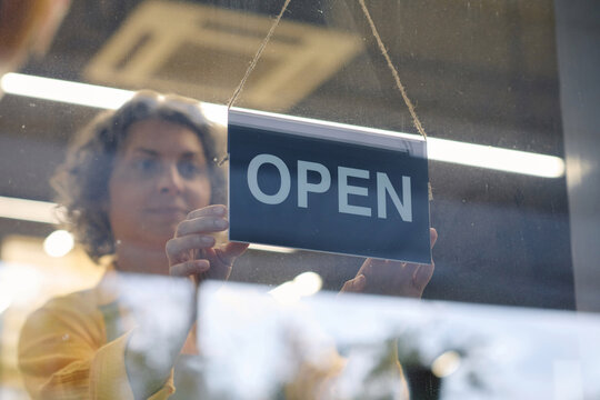 Store worker hanging Closed sign on glass door to close her store