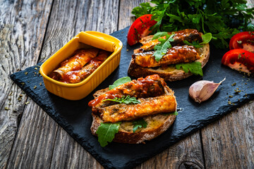 Tasty sandwiches - toasted bread with smoked sardine in tomato sauce on wooden table
