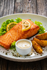 Seared salmon steak with baked potatoes and fresh vegetable salad served on wooden table

