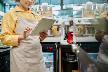 Manager of supermarket in apron working online on digital tablet