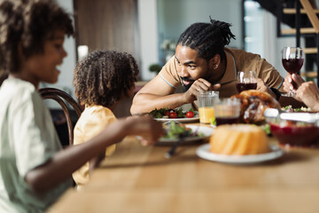 African American father having a meal with his small daughter and talking with her in a dining room