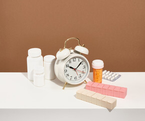 Vintage white alarm clock on the table. Pills and capsules in medical jars. Taking medication at certain times and on certain days.