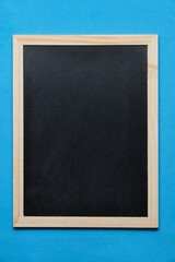 Black blackboard for notes in wooden frame blue background.