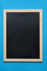 Fototapeta premium Black blackboard for notes in wooden frame blue background.