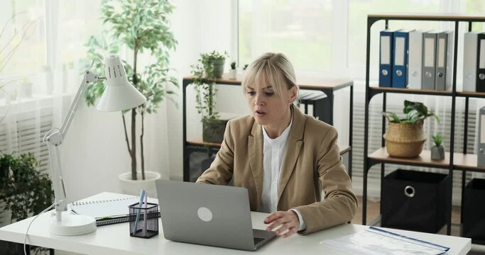 An angry woman office worker is seen getting frustrated and upset, leading her to close her laptop abruptly. Her facial expressions clearly express negative emotions in response to a disappointing.