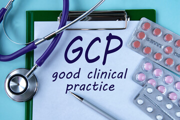 GCP - acronym on a white piece of paper on a blue background. A stethoscope and pills lie side by...