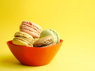 Macarons in a red bowl, yellow background and copy space.