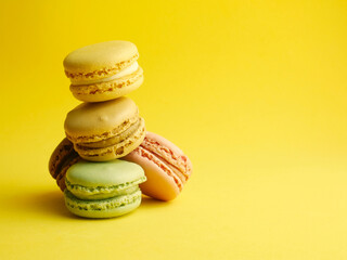 Fototapeta na wymiar Stacked macaroons, french sweet on yellow background, copy space.