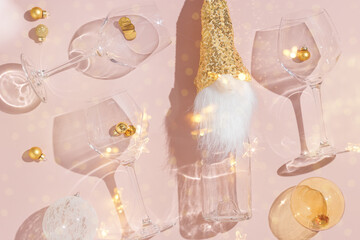 Happy New Year and Christmas holiday flat lay pattern, sparkling wine champagne bottle and wine glasses, xmas transparent balls on pink background. Cute dwarf in sequins hat as bottle decor